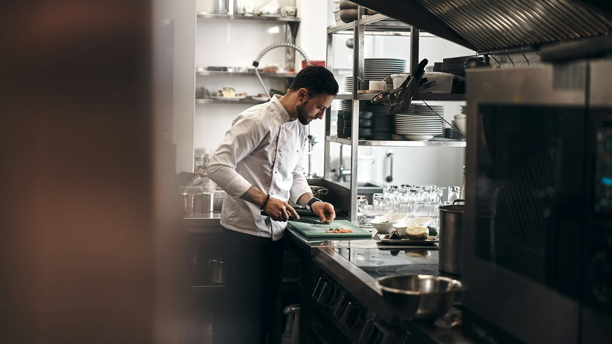 A chef in a white coat chops vegetables in a restaurant kitchen